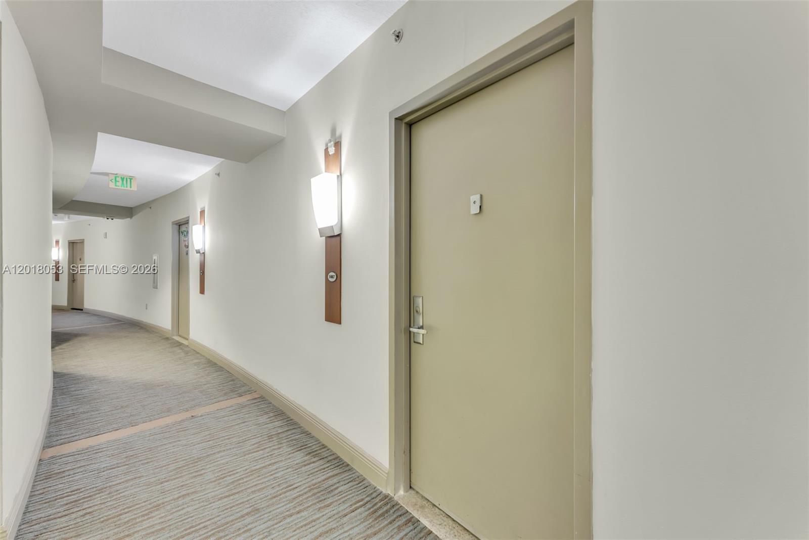 A hallway with beige walls, carpeted flooring, wall-mounted light fixtures, and several closed doors — 1750 N Bayshore Dr # 1407, Miami FL 33132, MIAMI, FL
