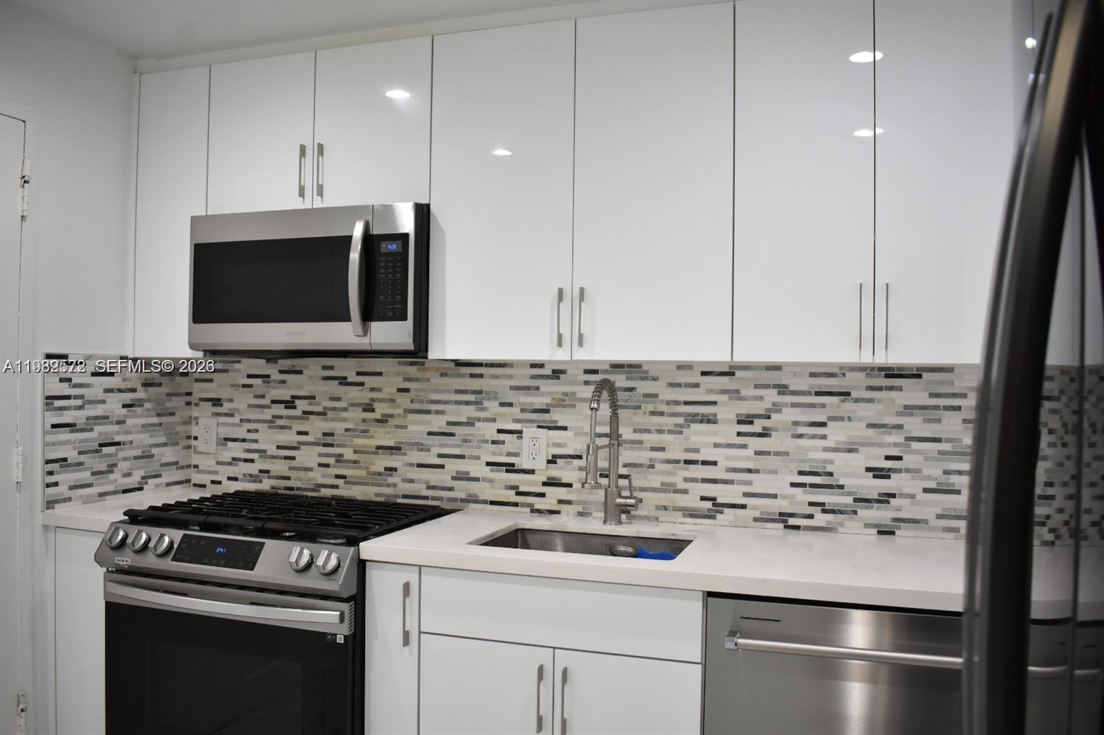 A kitchen features white cabinets, stainless steel appliances, and a multi-colored mosaic tile backsplash — 8024 Tatum Waterway Dr # 5A, Miami Beach FL 33141, MIAMI BEACH, FL