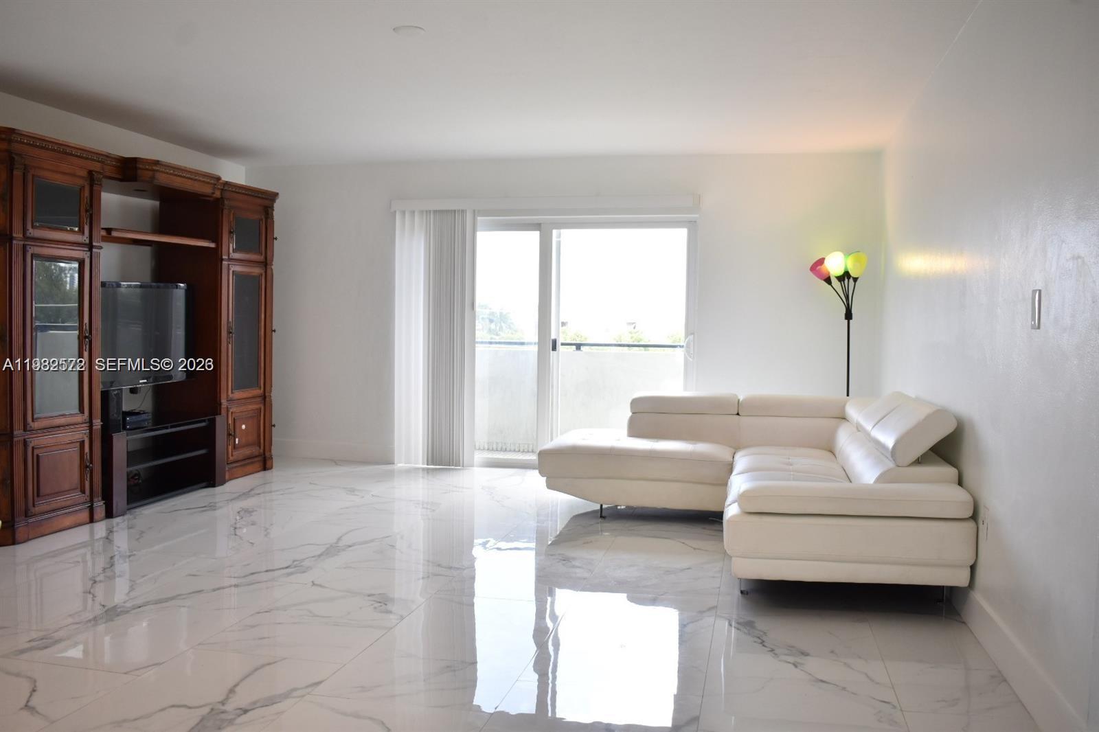 A living room features white marble floors, a large wooden entertainment center, and a sectional sofa — 8024 Tatum Waterway Dr # 5A, Miami Beach FL 33141, MIAMI BEACH, FL