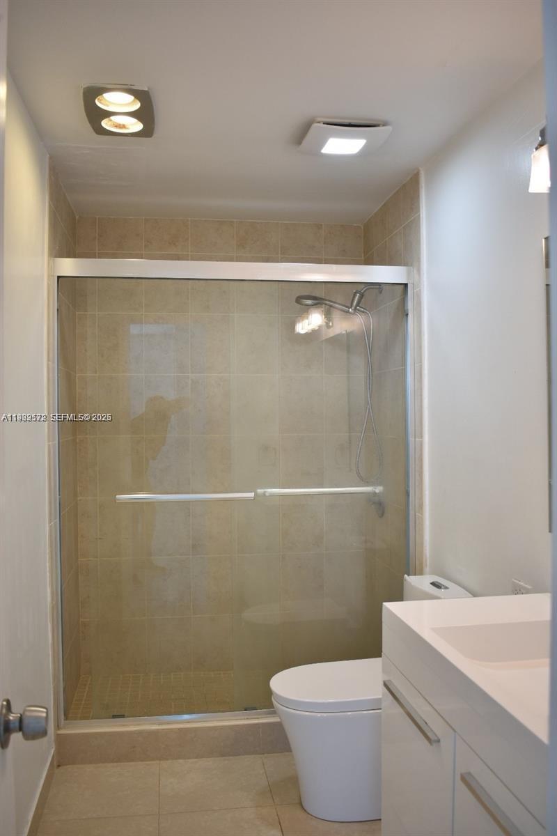 A bathroom features a glass-enclosed shower with beige tile, a white vanity, and a toilet — 8024 Tatum Waterway Dr # 5A, Miami Beach FL 33141, MIAMI BEACH, FL