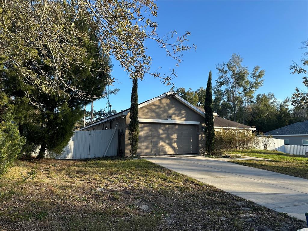 A tan single-story house with a two-car garage and a white vinyl fence — 11382 MAHOPAC ROAD, WEEKI WACHEE, FL