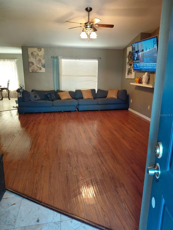 A living room with wood flooring, a blue sectional sofa, and a ceiling fan — 11382 MAHOPAC ROAD, WEEKI WACHEE, FL