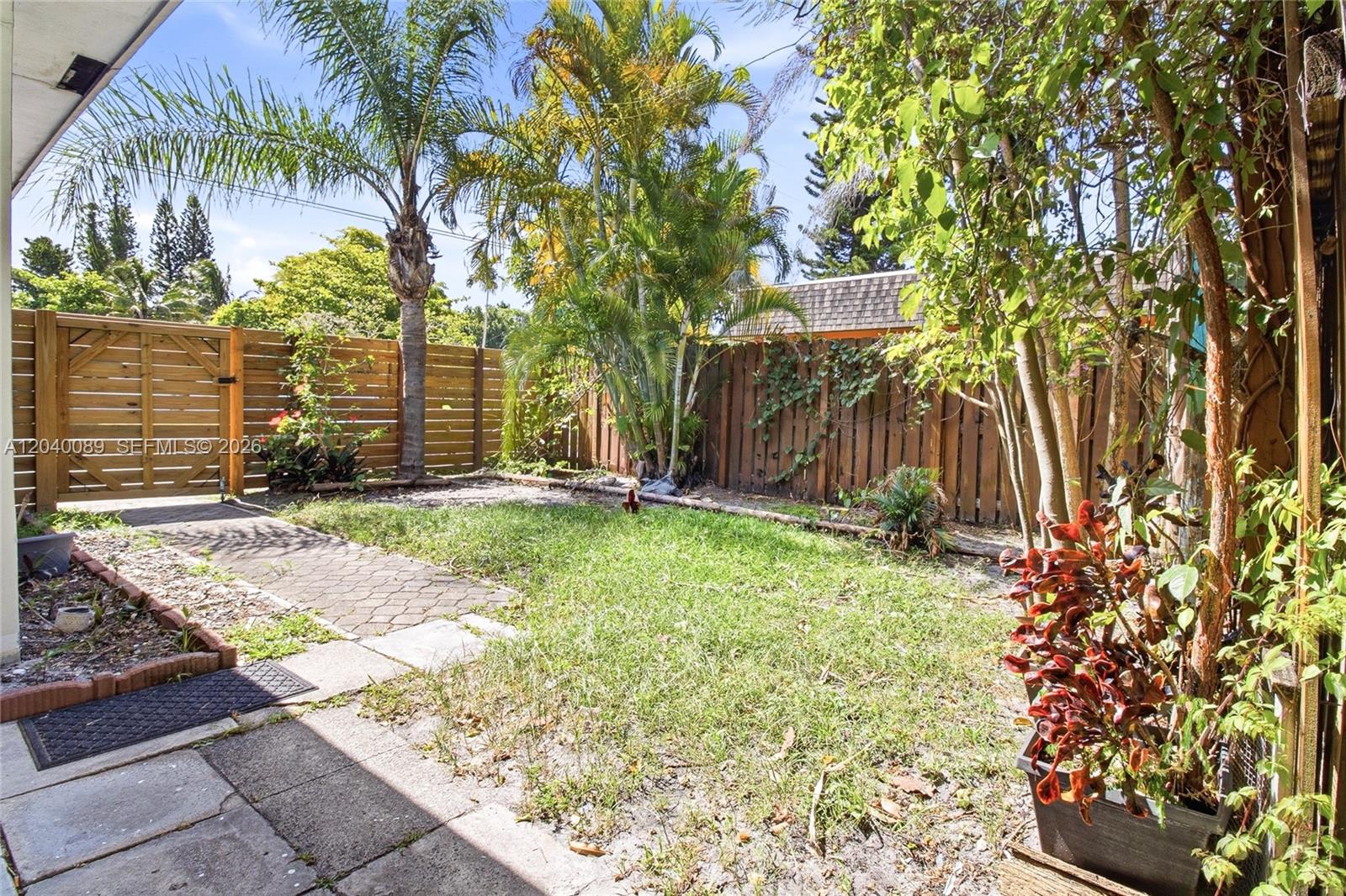 A fenced backyard features a small lawn, a paved walkway, and several palm trees — 610 SW 2nd Ave # 1, Dania Beach FL 33004, DANIA BEACH, FL