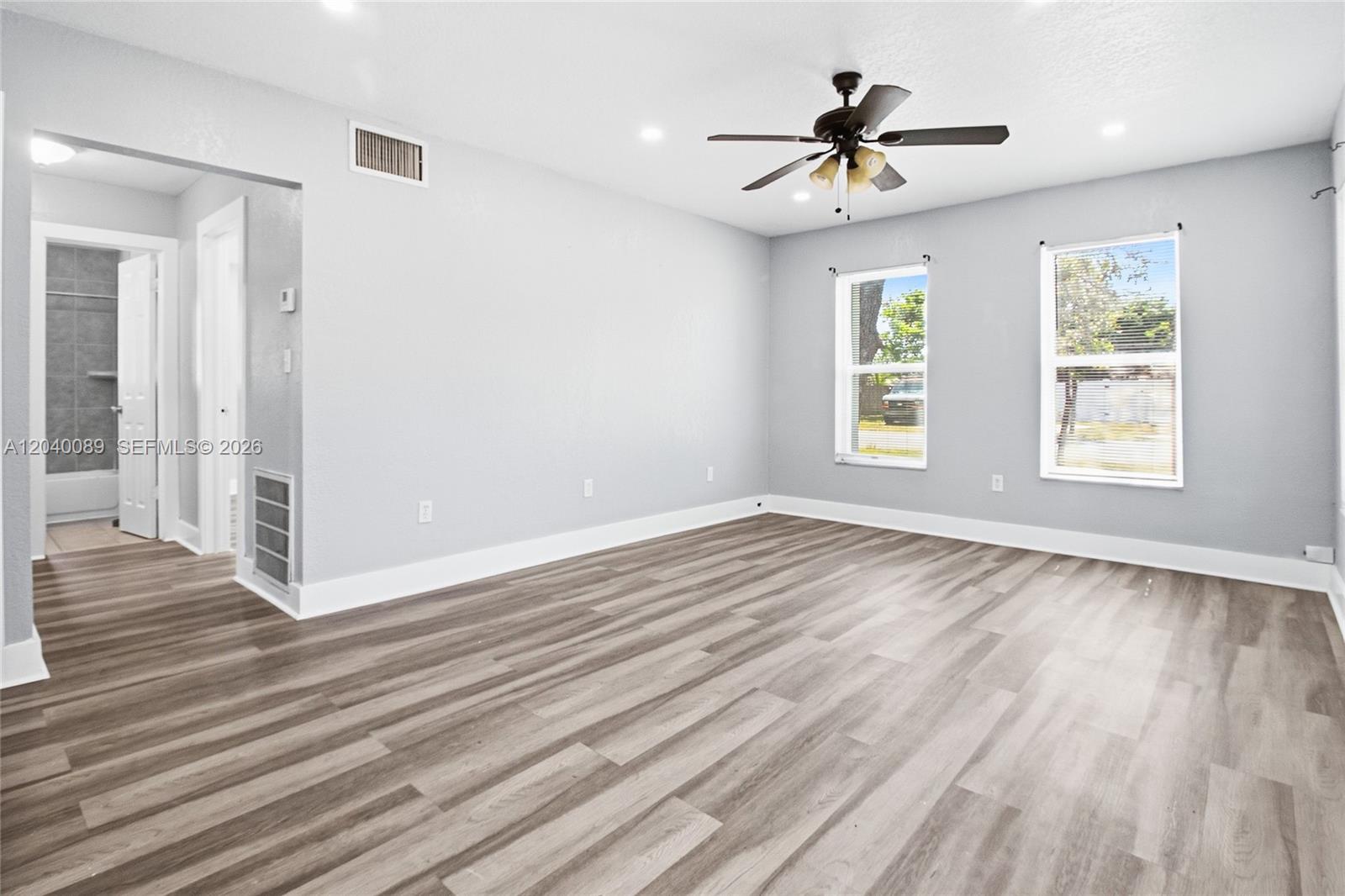 A bedroom with light gray walls, wood-look flooring, two windows, and an attached bathroom — 610 SW 2nd Ave # 1, Dania Beach FL 33004, DANIA BEACH, FL