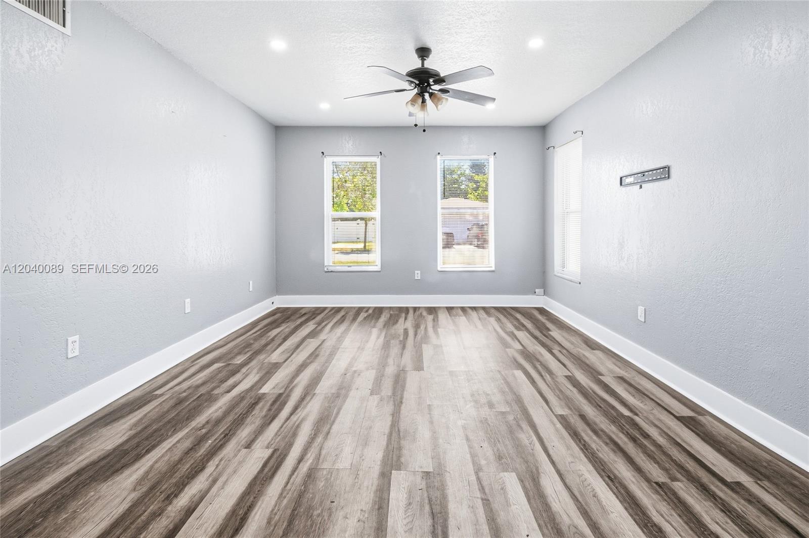 An empty room features light gray walls, wood-look flooring, two windows, and a ceiling fan — 610 SW 2nd Ave # 1, Dania Beach FL 33004, DANIA BEACH, FL
