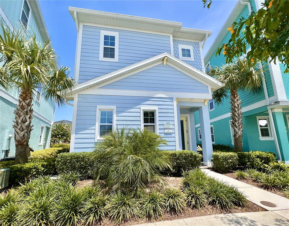 A light blue two-story house with a front porch and palm trees in the yard — 8067 KNEE DEEP ROAD, KISSIMMEE, FL