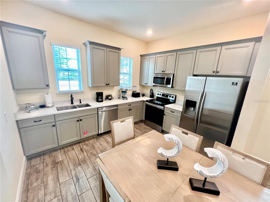 A kitchen features gray cabinets, stainless steel appliances, white countertops, and a dining table — 8067 KNEE DEEP ROAD, KISSIMMEE, FL