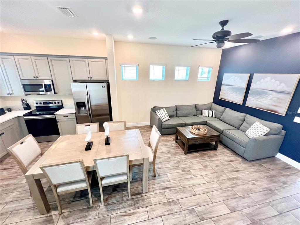 An open-concept kitchen and living room features light wood flooring, gray cabinetry, and a sectional — 8067 KNEE DEEP ROAD, KISSIMMEE, FL