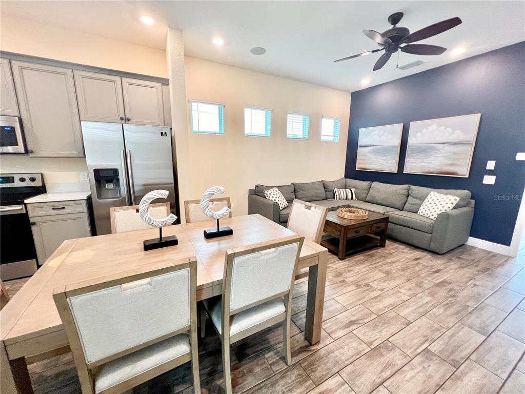 An open-concept kitchen and living area features a dining table, gray sectional, and wood-look flooring — 8067 KNEE DEEP ROAD, KISSIMMEE, FL