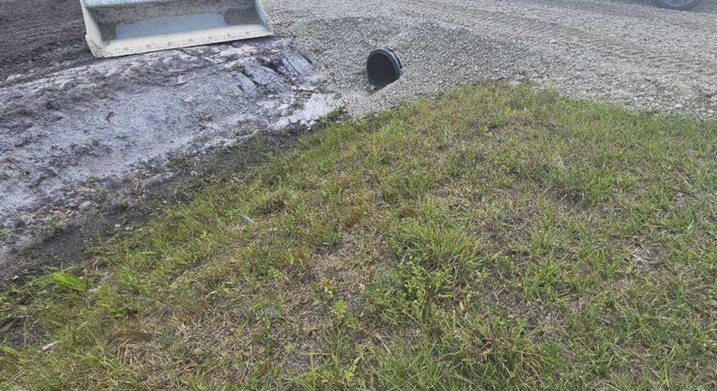 A black drainage pipe protrudes from a gravel driveway next to a grassy yard — 17926 NW 250TH STREET, OKEECHOBEE, FL