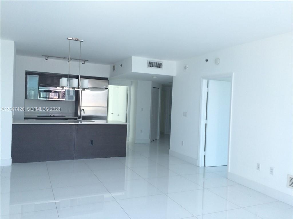 A modern kitchen with stainless steel appliances overlooks a bright, white-tiled living area — 55 SE 6th St # 2807, Miami FL 33131, MIAMI, FL