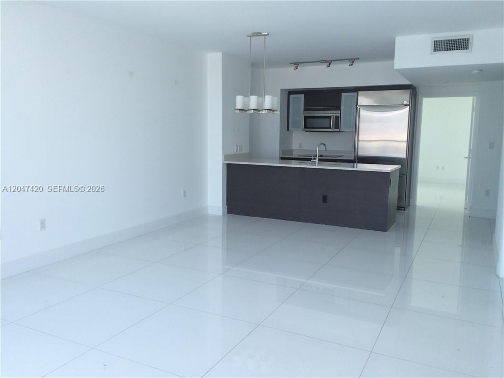A modern kitchen with dark cabinetry and stainless steel appliances overlooks an open living area — 55 SE 6th St # 2807, Miami FL 33131, MIAMI, FL