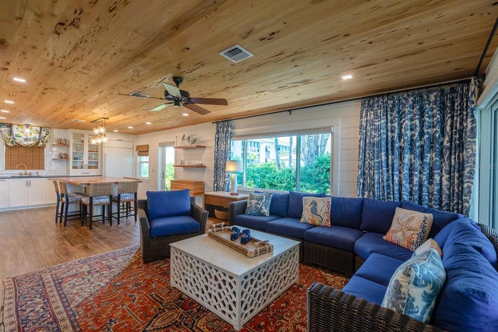 A living room with a wood-plank ceiling, blue sectional sofa, and a large patterned rug — 6020 MIDNIGHT PASS ROAD UNIT 26, SARASOTA, FL
