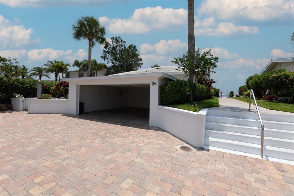 A paved driveway leads to a covered carport with white walls and a house number — 6020 MIDNIGHT PASS ROAD UNIT 26, SARASOTA, FL