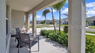A covered front porch features two chairs and a view of a suburban neighborhood street — 16747 SUNBURST LAKE STREET, WIMAUMA, FL