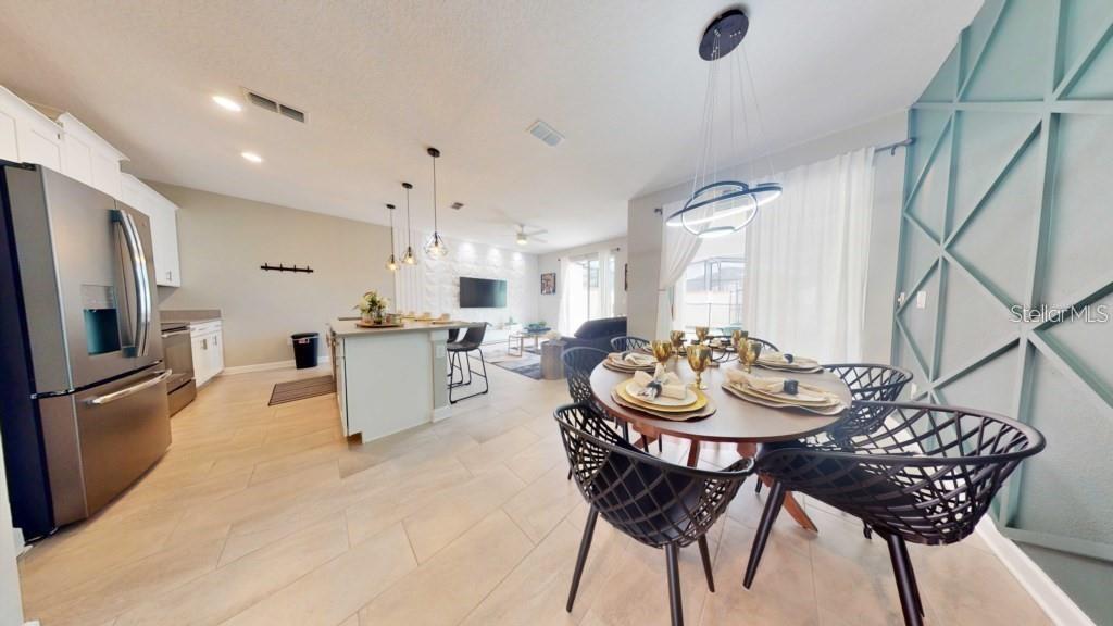 A dining area with a round table and black chairs opens into a modern kitchen — 4830 MEMORIES LANE, KISSIMMEE, FL