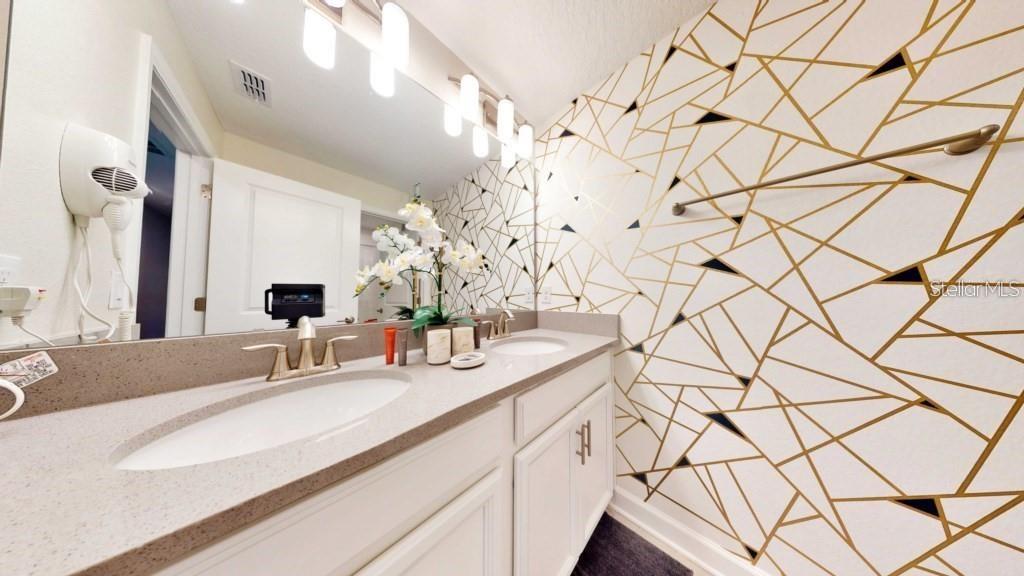 A bathroom features a double vanity with a geometric gold and white wallpaper accent wall — 4830 MEMORIES LANE, KISSIMMEE, FL