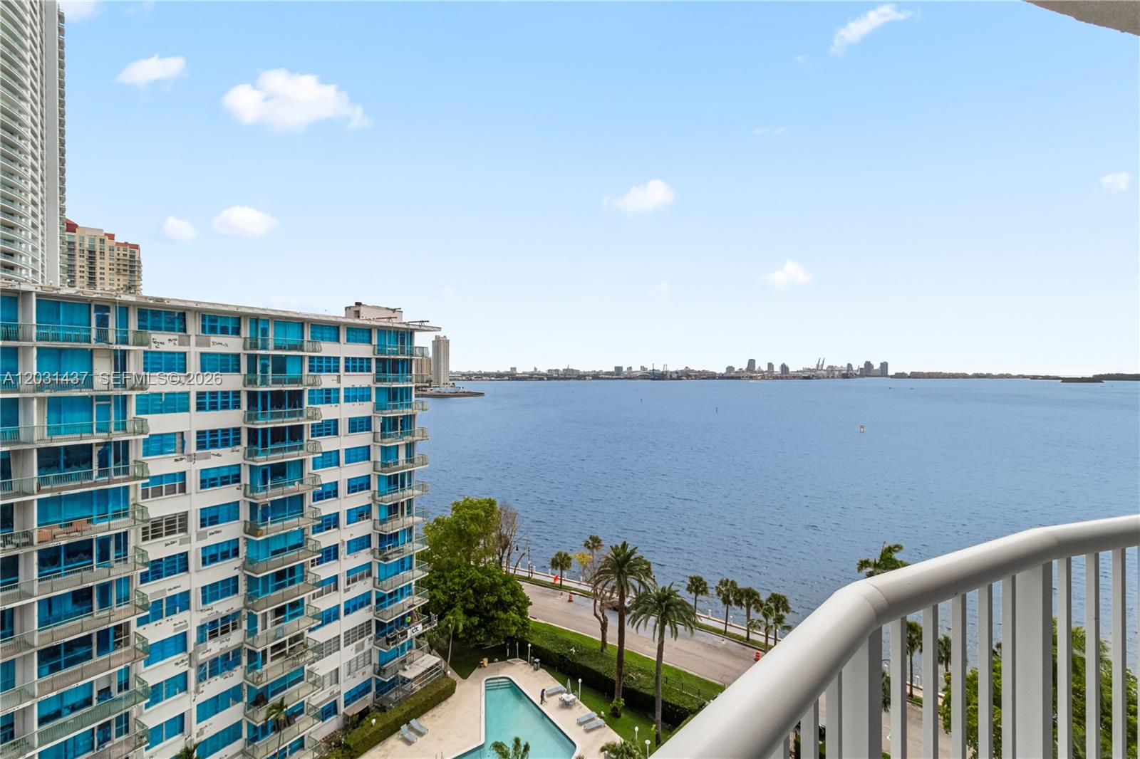 A high-rise balcony overlooks a swimming pool, a coastal road, and a bay with city skylines — 1420 Brickell Bay Dr # 1405C, Miami FL 33131, MIAMI, FL