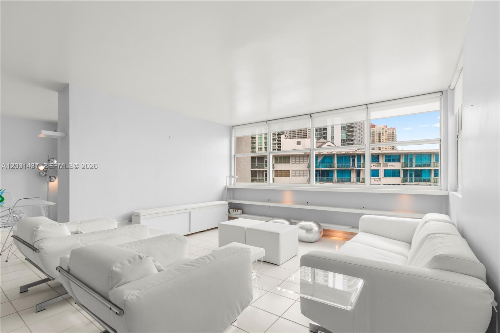 A bright living room features white furniture, tiled floors, and large windows overlooking city buildings — 1420 Brickell Bay Dr # 1405C, Miami FL 33131, MIAMI, FL