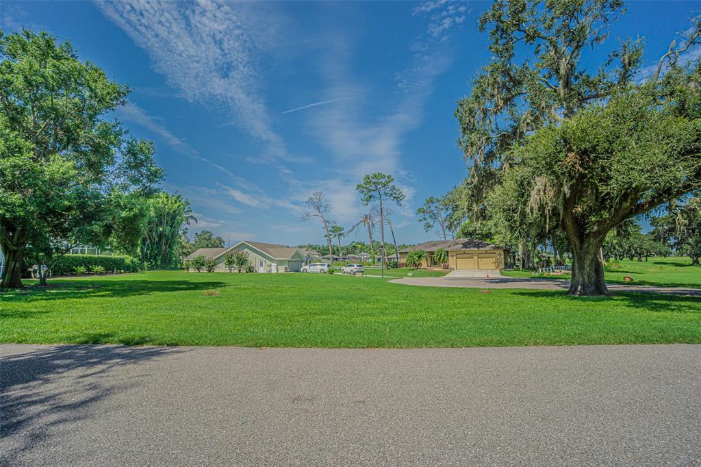 A wide, grassy lawn sits in front of two suburban houses under a blue sky — BRENTWOOD DRIVE, ZEPHYRHILLS, FL