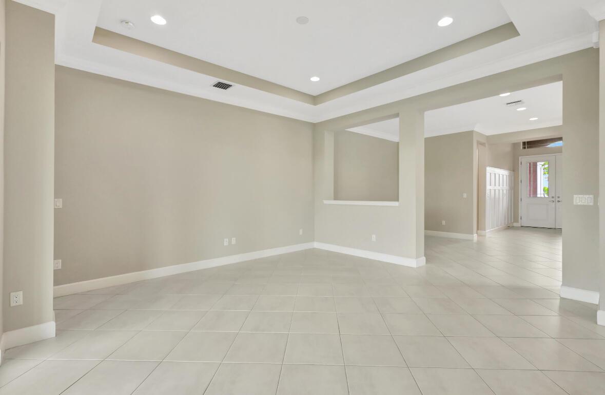 An empty living room with light tile flooring, neutral walls, and a tray ceiling — 15684 Goldfinch Circle, FL 33470, FL
