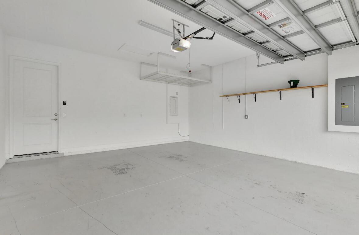 An empty garage with white walls, a gray floor, overhead storage, and a wooden shelf — 15684 Goldfinch Circle, FL 33470, FL