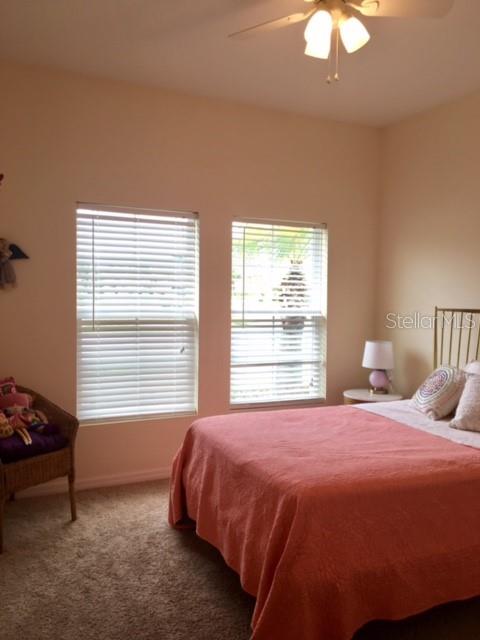 A bedroom features a bed with a coral quilt, two windows with blinds, and a chair — 7903 PLEASANT PINE CIRCLE, WINTER PARK, FL