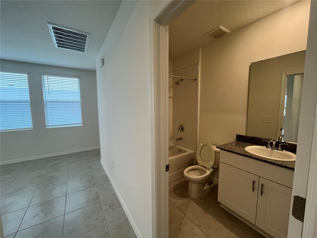 A tiled room leads into a bathroom with a vanity, toilet, and shower-tub combination — 3889 GIORGIO DRIVE, WINTER HAVEN, FL