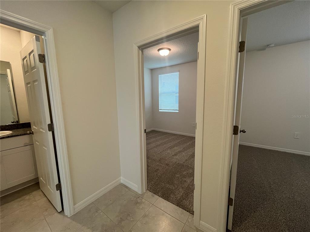 A hallway with tile flooring leads to a bathroom and two carpeted bedrooms — 3889 GIORGIO DRIVE, WINTER HAVEN, FL