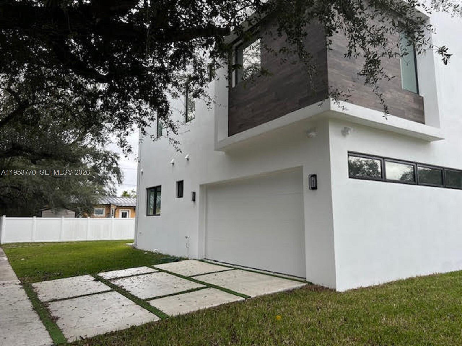 A modern two-story house features a white exterior, a garage, and wood-paneled upper accents — 2 Hough Dr, Miami Springs FL 33166, MIAMI SPRINGS, FL