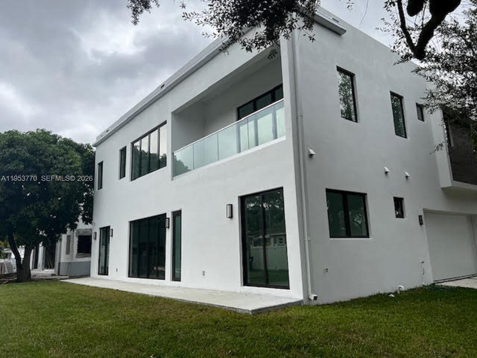 A two-story white modern house features a glass balcony, large windows, and a concrete patio — 2 Hough Dr, Miami Springs FL 33166, MIAMI SPRINGS, FL