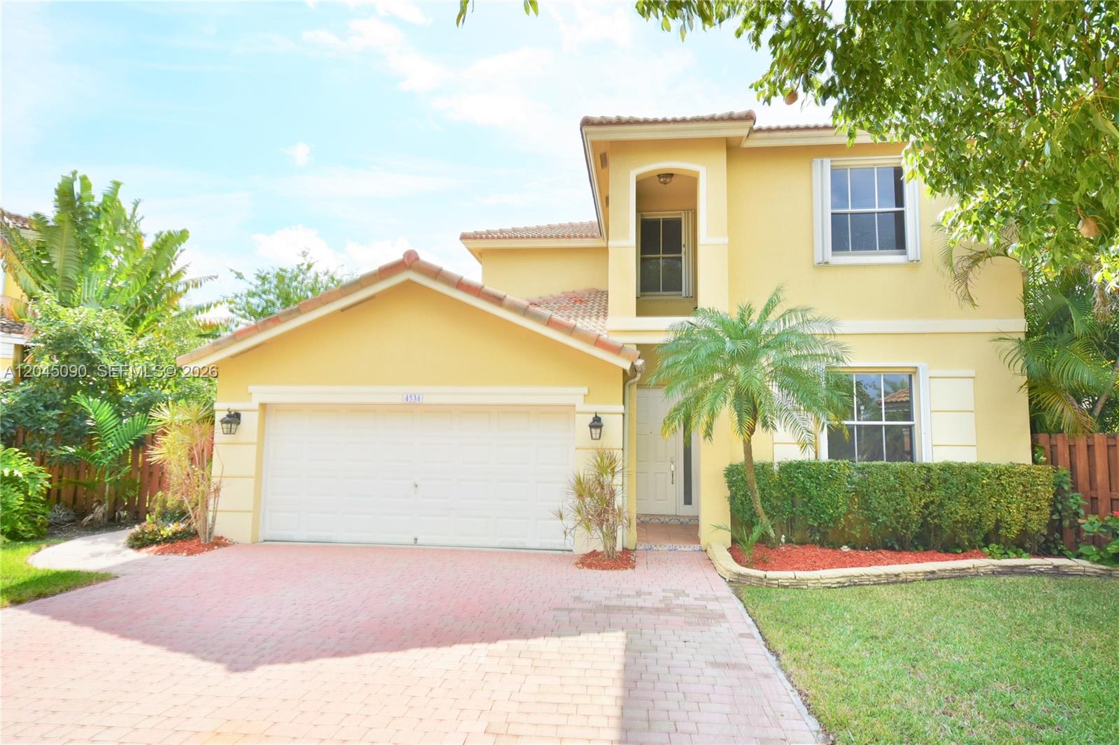 A two-story yellow stucco house features a two-car garage and a paved driveway — 4534 NW 94th Pl, Doral FL 33178, DORAL, FL