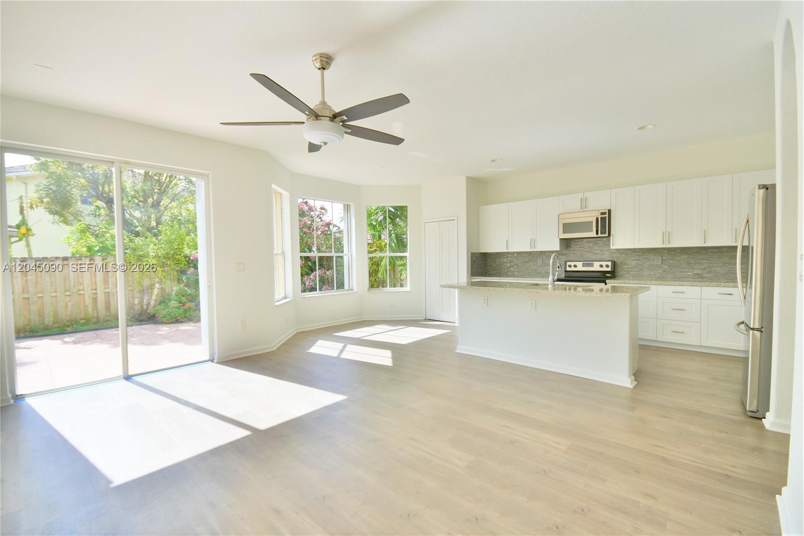 An open-concept kitchen and living area features white cabinetry, stainless steel appliances, and sliding glass doors — 4534 NW 94th Pl, Doral FL 33178, DORAL, FL