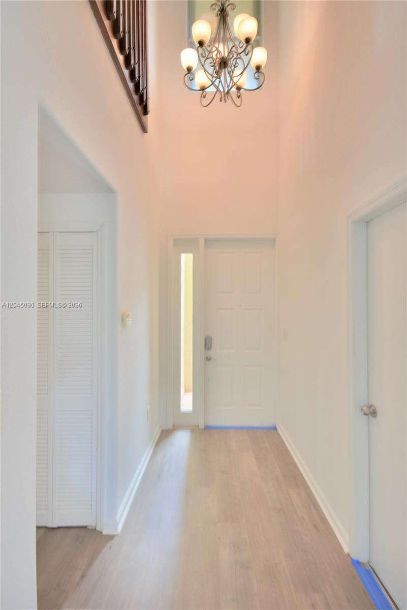 A bright entryway features light wood flooring, a white door with a sidelight, and a chandelier — 4534 NW 94th Pl, Doral FL 33178, DORAL, FL