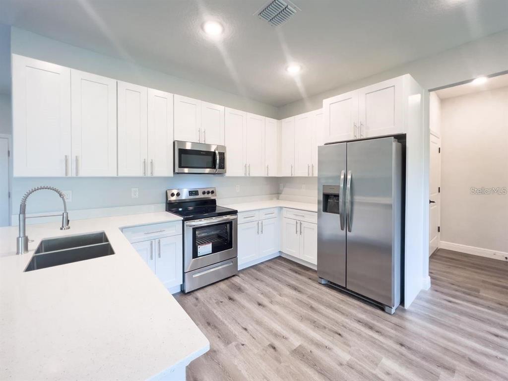 A kitchen with white cabinets, stainless steel appliances, and light wood-look flooring — 1580 EAST PARKWAY, DELAND, FL