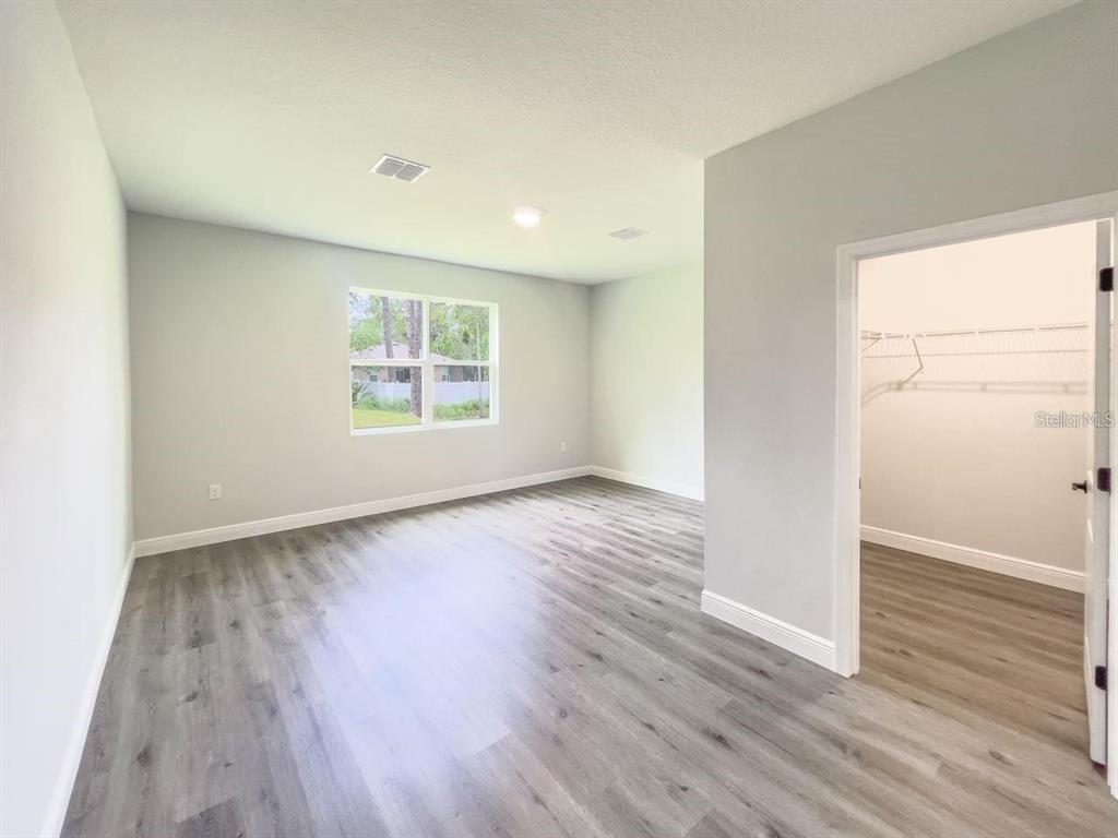 A bedroom with gray walls, wood-look flooring, a window, and an attached walk-in closet — 1580 EAST PARKWAY, DELAND, FL