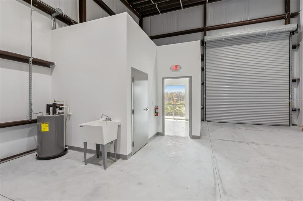 An industrial warehouse space features a utility sink, water heater, and an exterior exit door — 7120 SAMPEY ROAD UNIT 106, GROVELAND, FL