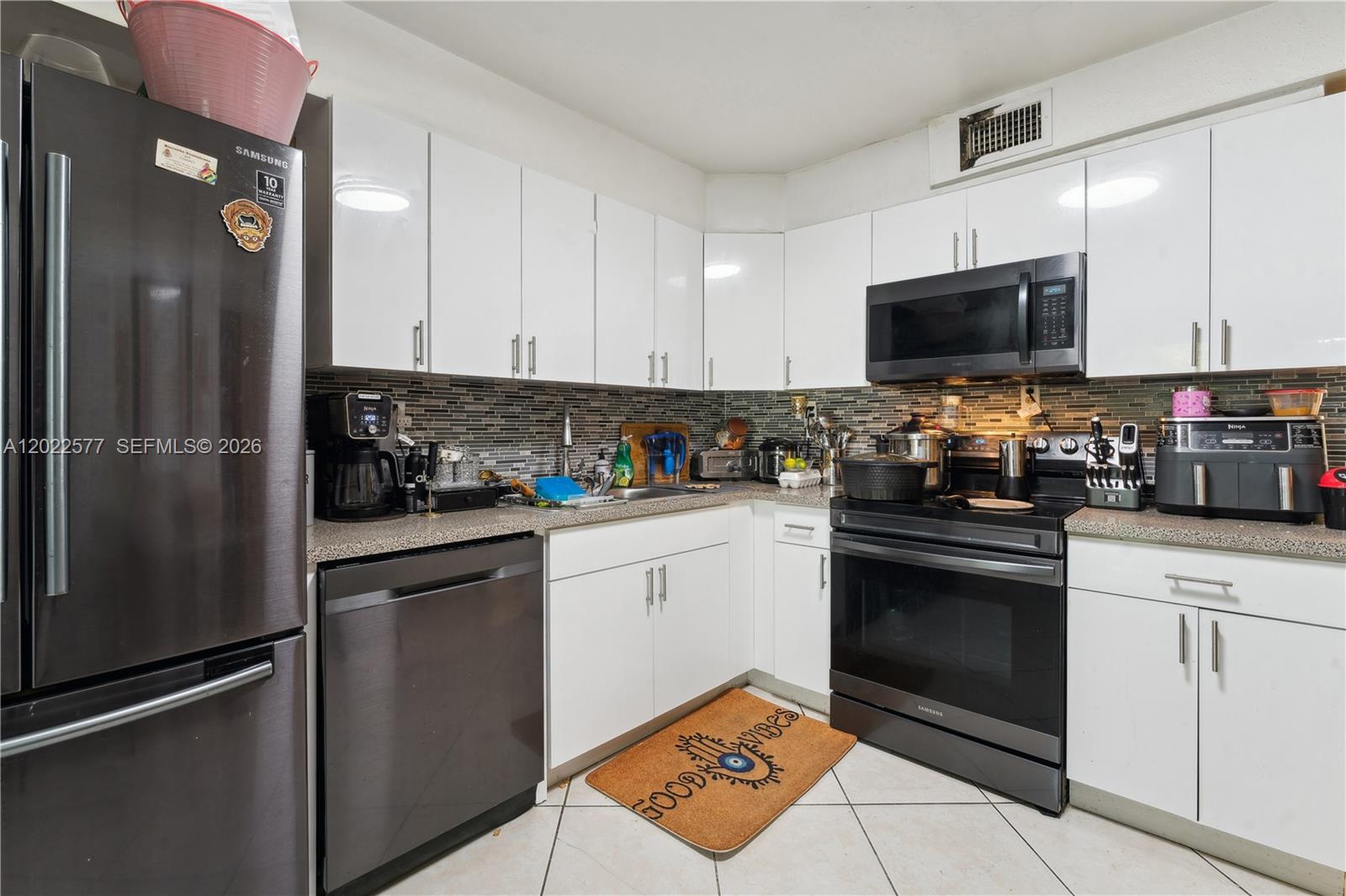 A kitchen features white cabinets, dark appliances, a tiled backsplash, and light-colored floor tiles — MIAMI, FL
