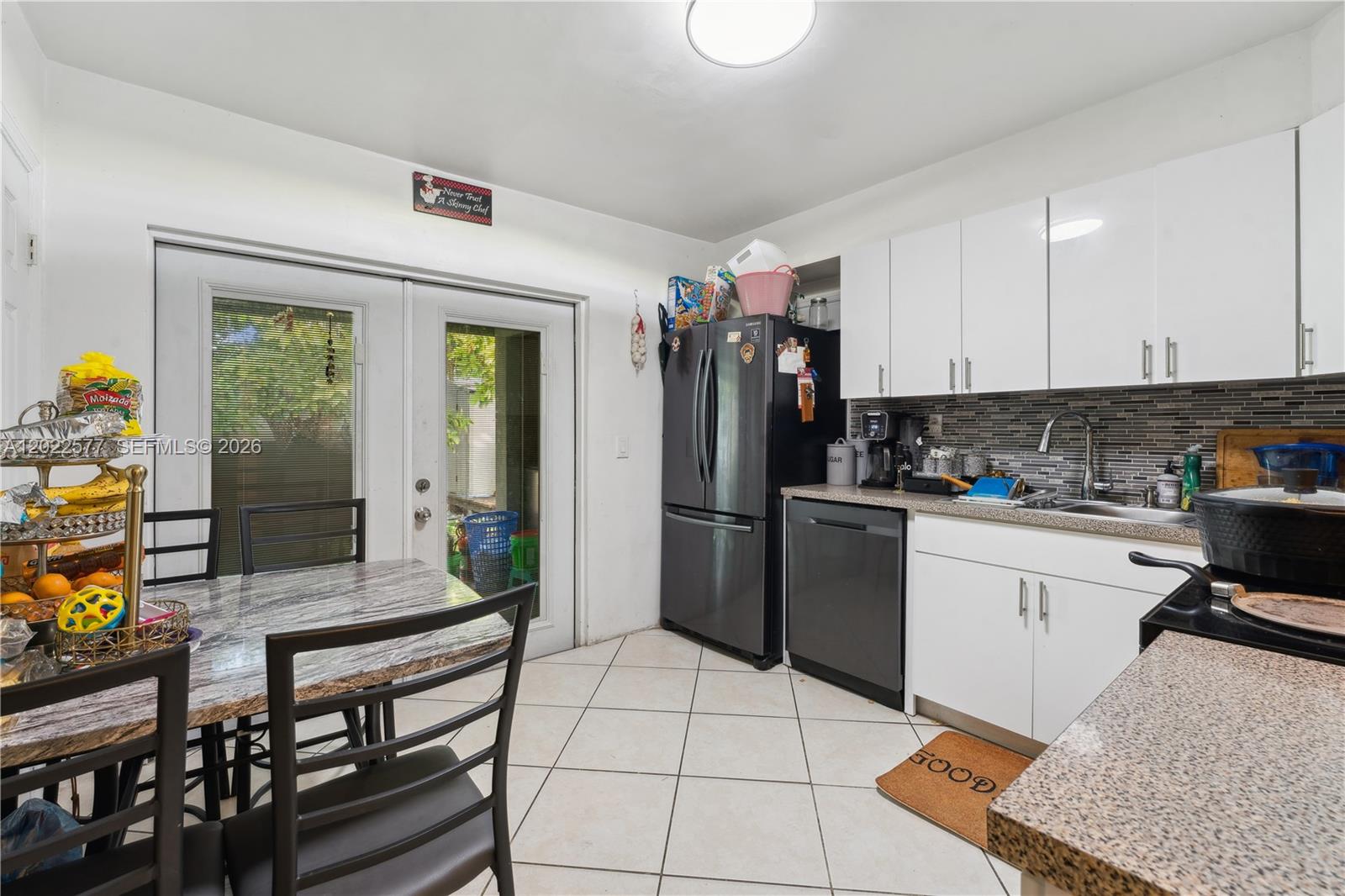 A kitchen features white cabinets, a dark refrigerator, a dishwasher, and a dining table — MIAMI, FL