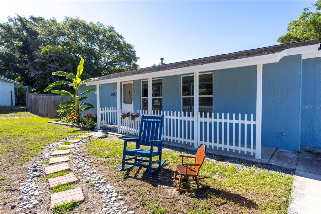 A blue house with a white picket fence and two rocking chairs on the lawn — 2877 NUTWOOD STREET, CLEARWATER, FL