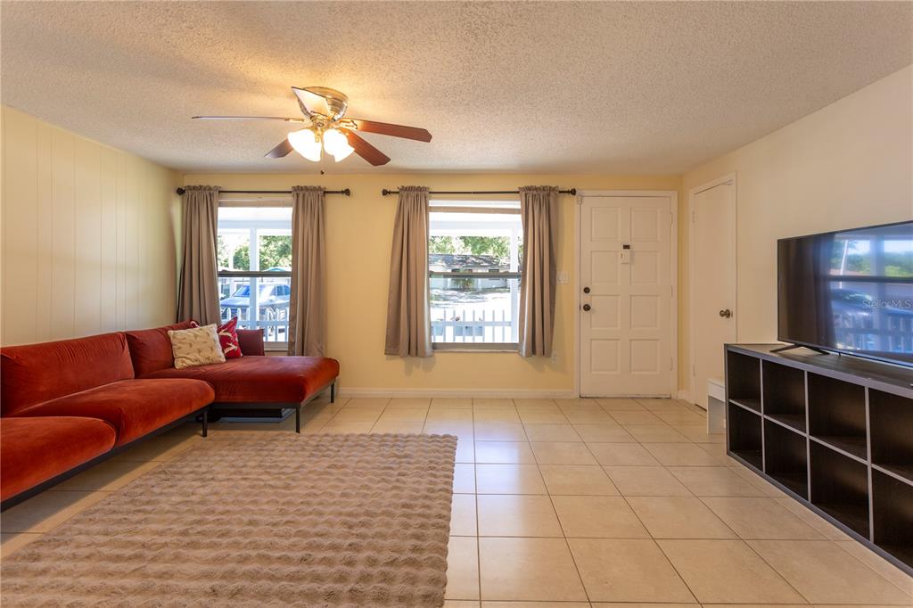 A living room features a red sectional sofa, a television on a shelf, and tiled floors — 2877 NUTWOOD STREET, CLEARWATER, FL