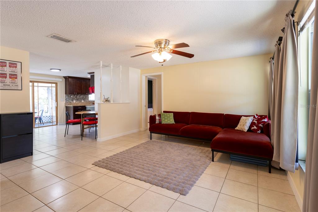 A living room with tile floors, a red sectional sofa, and an adjacent dining area — 2877 NUTWOOD STREET, CLEARWATER, FL