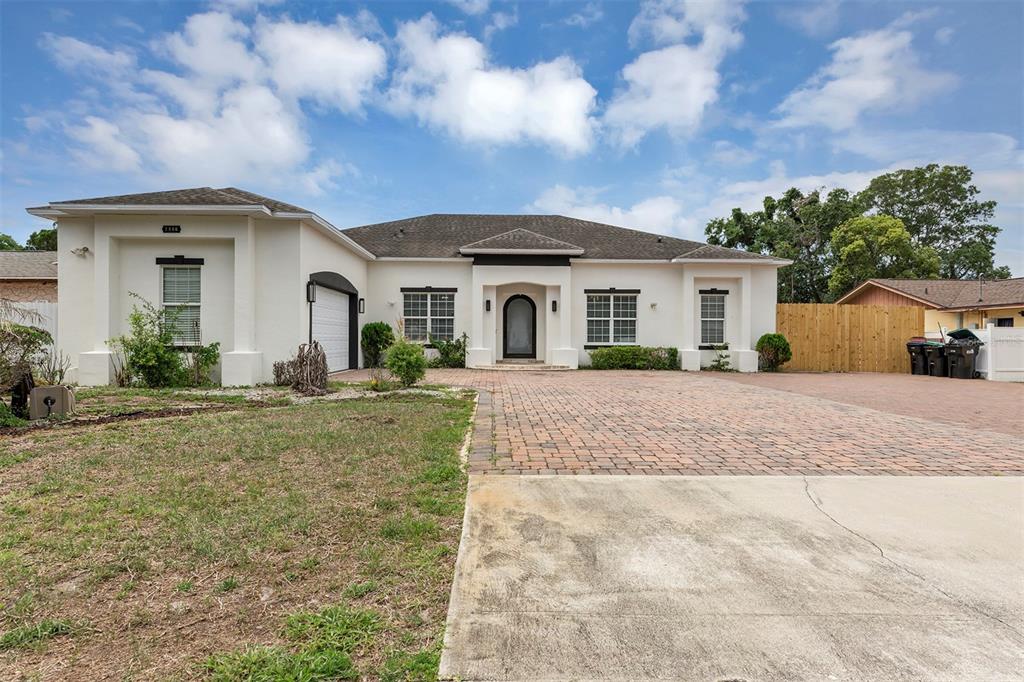 A single-story white stucco house features a brick paver driveway and a dark arched entryway — 7906 NAPOLEON STREET, ORLANDO, FL