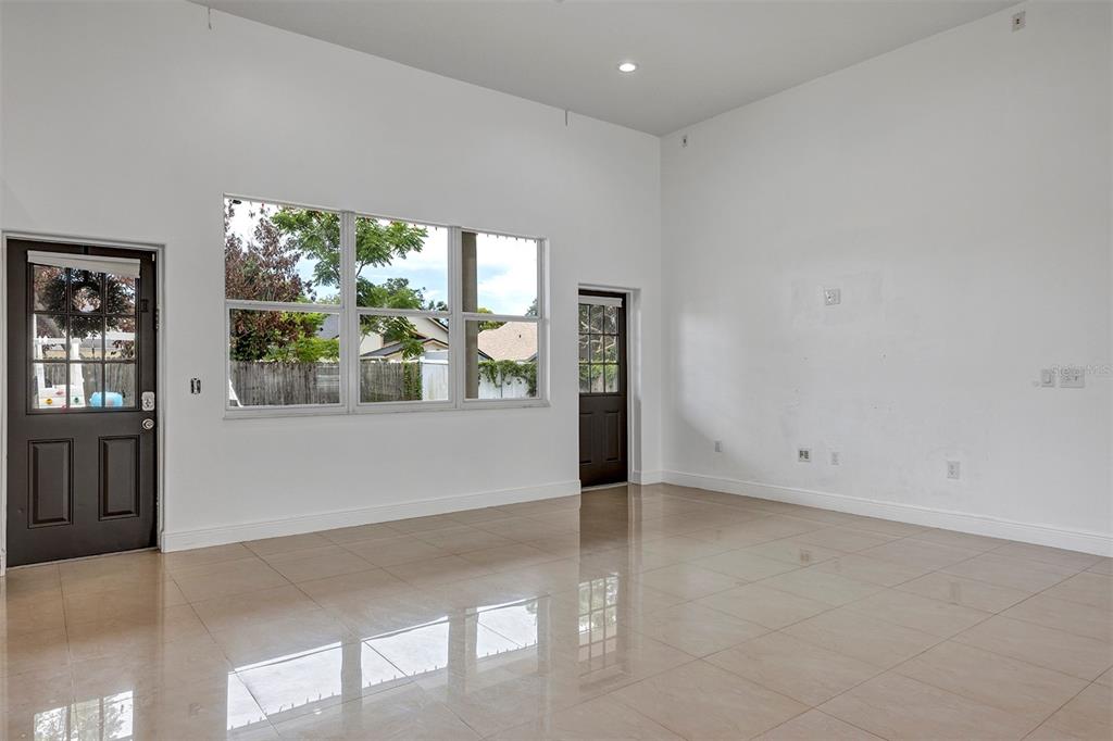 An empty room with high ceilings, tile floors, large windows, and two dark exterior doors — 7906 NAPOLEON STREET, ORLANDO, FL