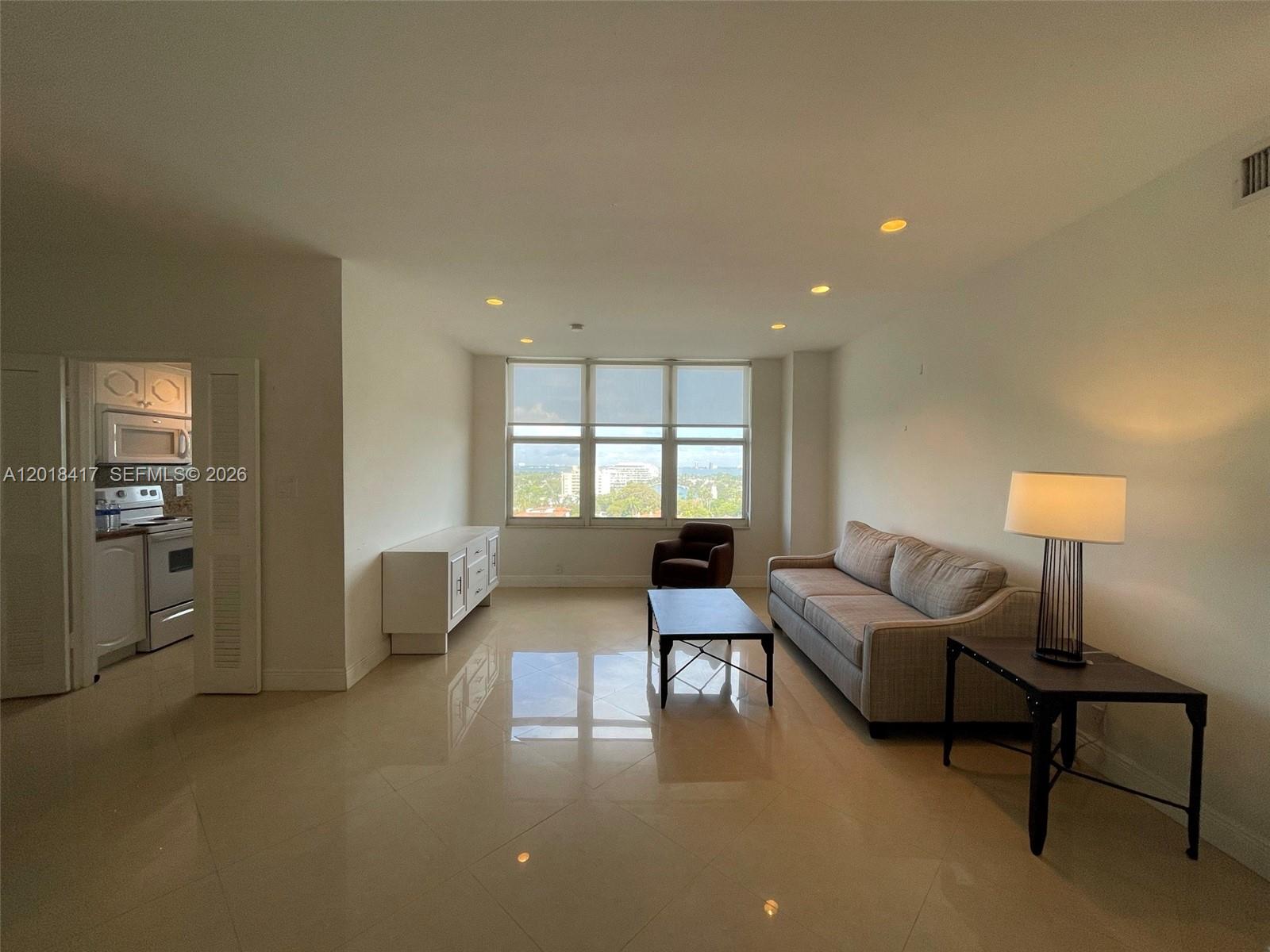 A living room with light tile floors, a beige sofa, and a view of the city — 4747 Collins Ave # 1102, Miami Beach FL 33140, MIAMI BEACH, FL