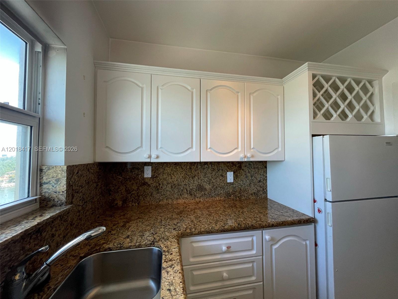 A kitchen features white cabinets, granite countertops, a stainless steel sink, and a refrigerator — 4747 Collins Ave # 1102, Miami Beach FL 33140, MIAMI BEACH, FL