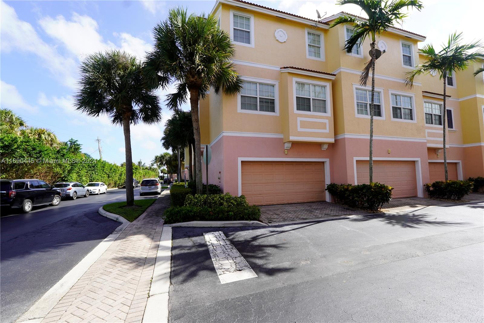 A three-story townhouse with a peach and yellow exterior features multiple garage doors and palms — 123 Harbors Way, Boynton Beach FL 33435, BOYNTON BEACH, FL