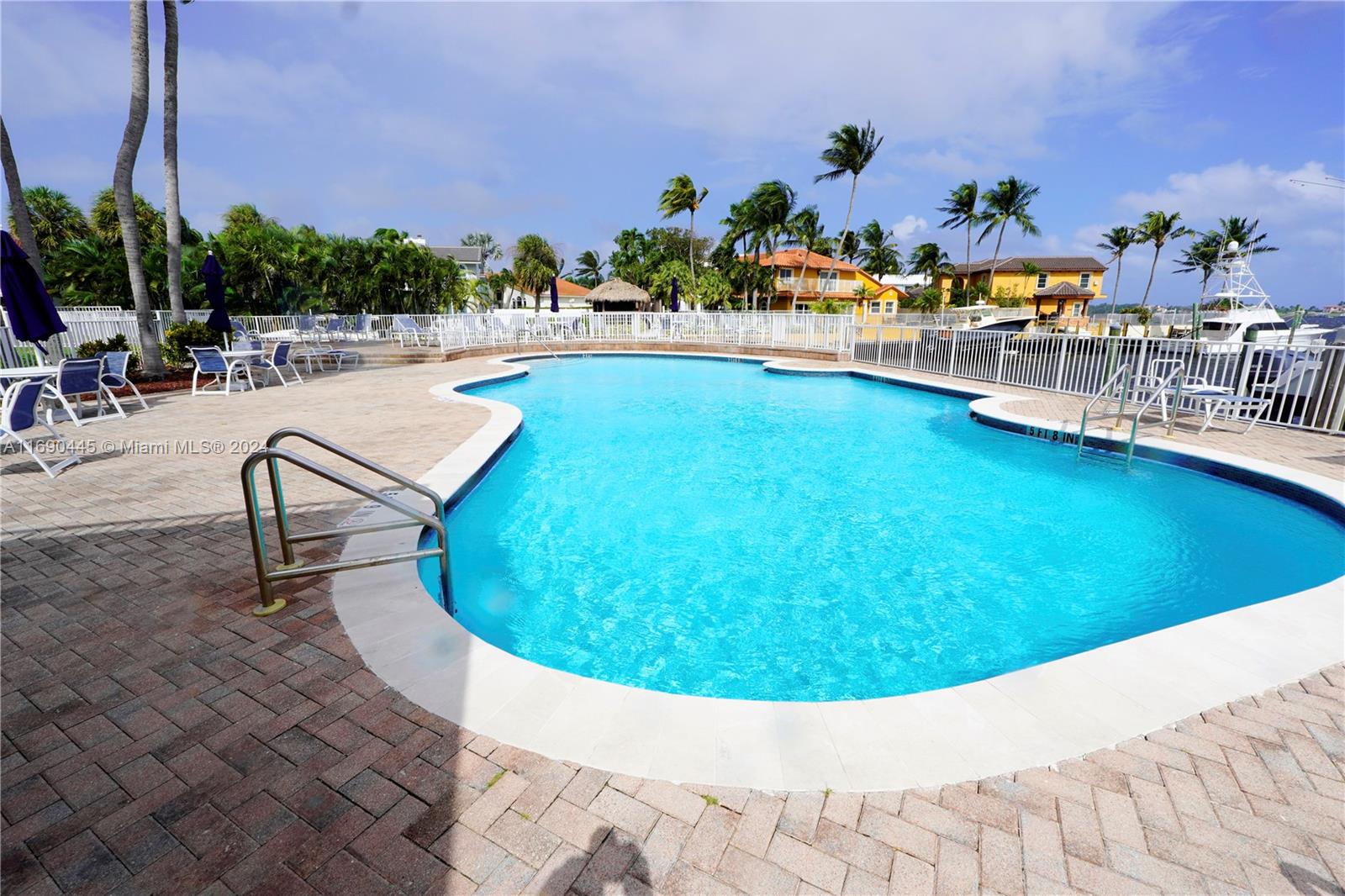 A swimming pool with a brick deck is surrounded by a white fence and palm trees — 123 Harbors Way, Boynton Beach FL 33435, BOYNTON BEACH, FL