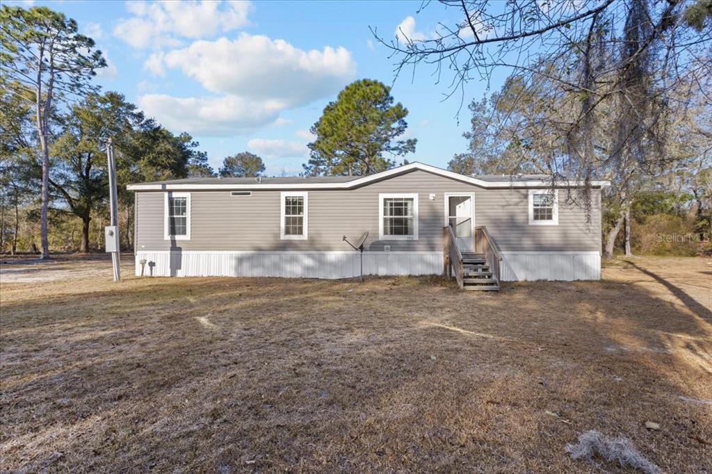 A single-story manufactured home with gray siding sits on a large, grassy lot — 1910 NE 155TH COURT, WILLISTON, FL