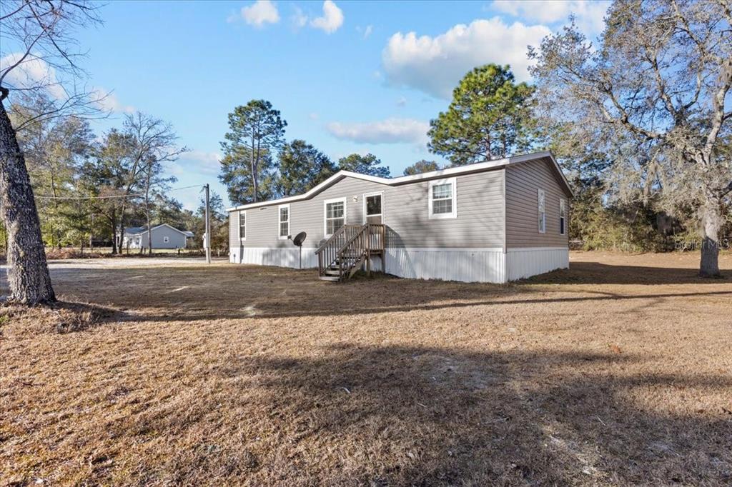 A gray manufactured home with white skirting sits on a large, grassy lot — 1910 NE 155TH COURT, WILLISTON, FL
